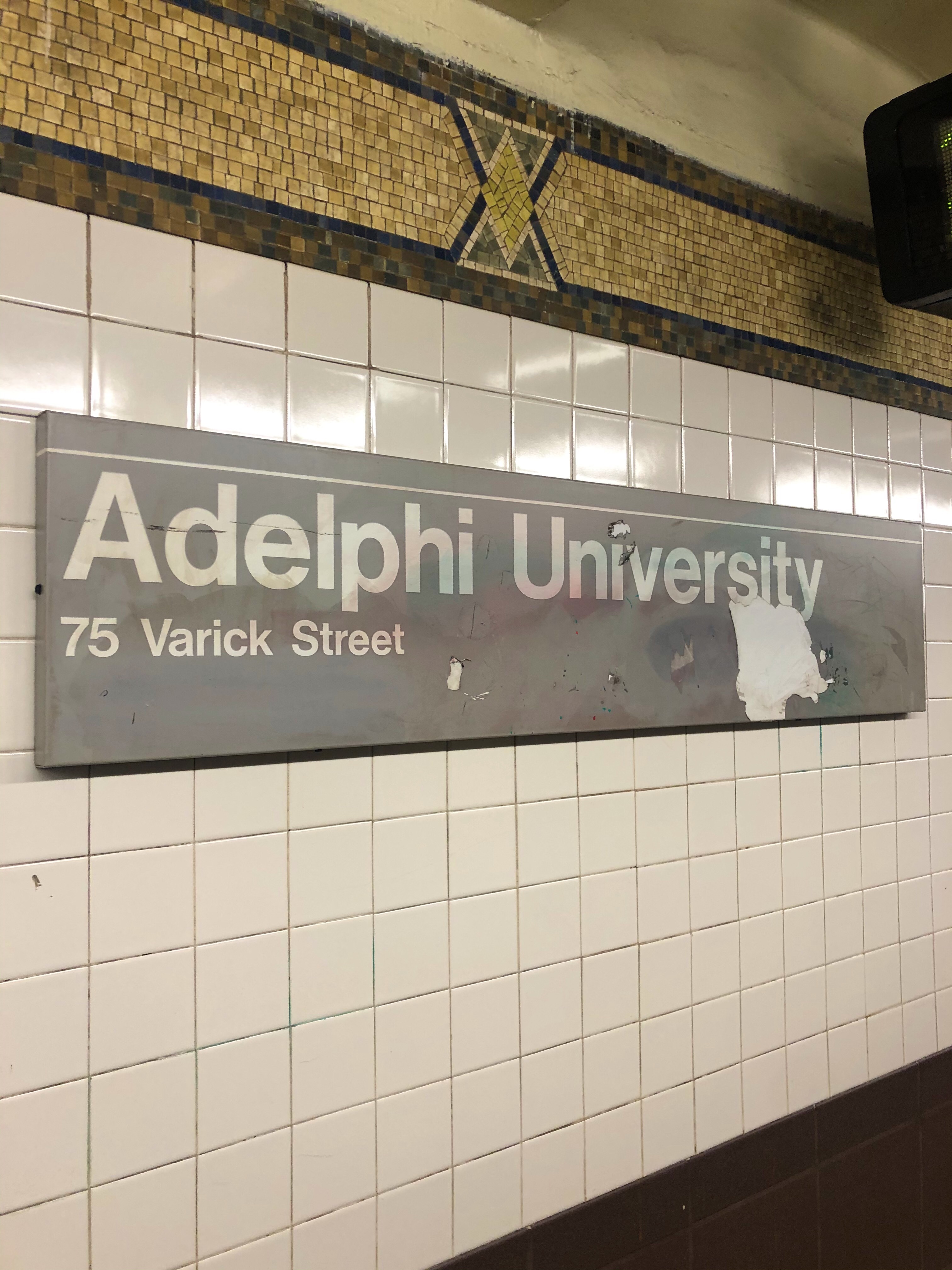 Subway sign that says "Adelphi University 75 Varick Street"